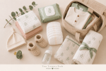 Soft flat lay of baby hospital bag essentials including newborn outfits, nappies, wipes, muslin cloths, baby blanket, booties, hat, pacifier and bottle.