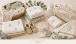 Soft flat lay of newborn laundry items including baby onesies, muslin cloths, blankets, towels, socks, booties, mesh laundry bag and baby detergent.